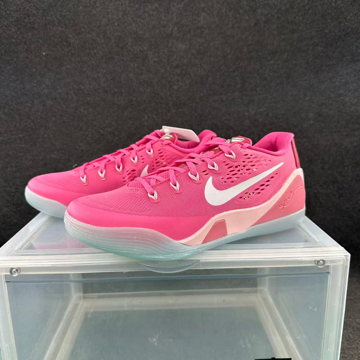 Pair of pink Nike basketball sneakers with white Swooshes displayed on a clear case.