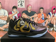 Side view of a Nike basketball sneaker with metallic gold detailing, a dark purple upper, and black midsole.