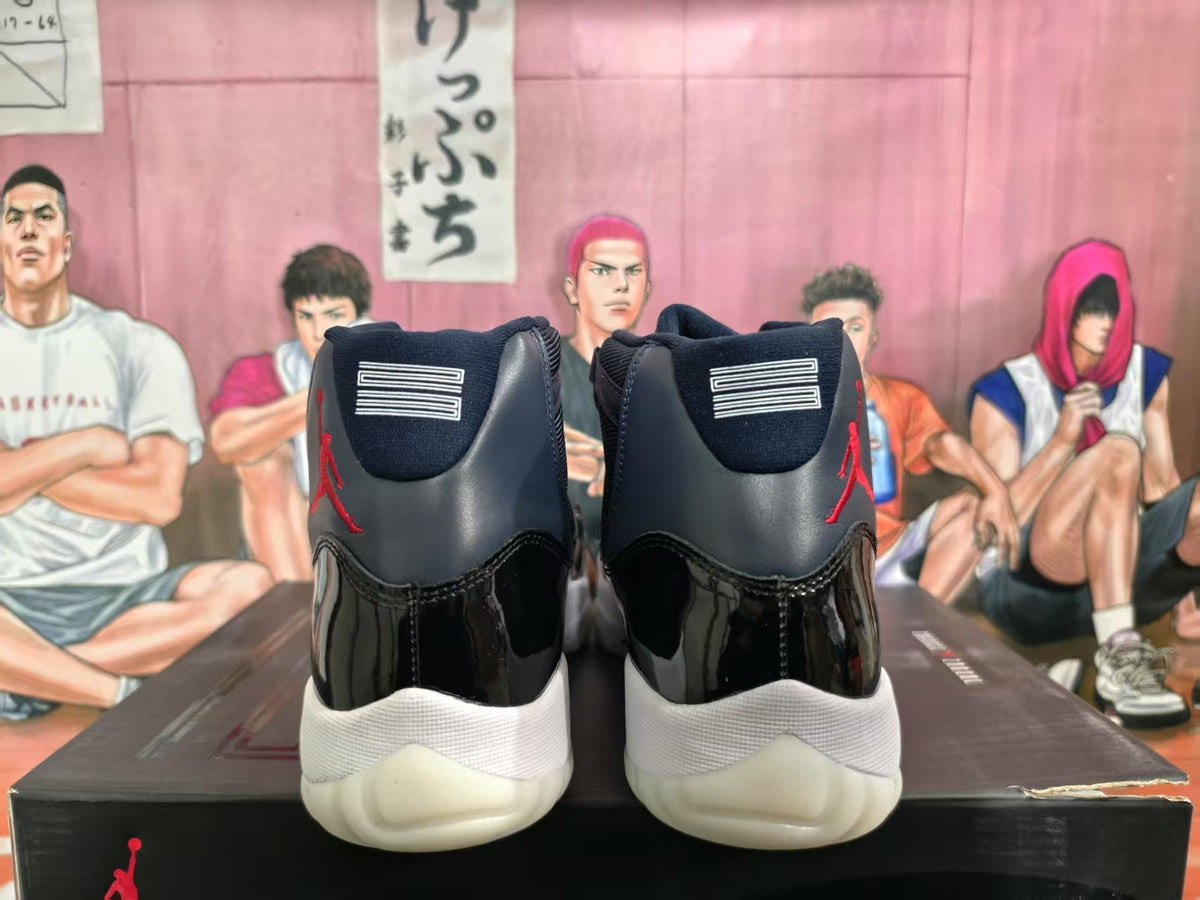 Rear view of black and dark blue high-top Jordan sneakers with red branding, white midsoles, and translucent outsoles on a branded box.
