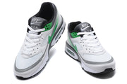 Front views of a pair of white sneakers with green accents and dark tongues.