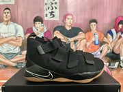Side profile of a black Nike basketball sneaker with adjustable straps, white Swoosh detailing, and a gum-colored outsole