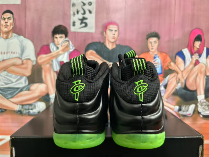 Rear view of black high-top sneakers with neon green outsoles and green tongue accents on a shoebox.