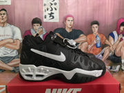 Side profile of a black Nike sneaker with a large white Swoosh, layered panels, and a white midsole.