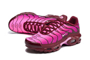 Angled view of pink Nike Air Max Plus sneakers with burgundy overlays