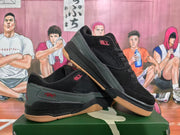 Angled view of a pair of black and dark green Jordan sneakers with red accents and gum-colored outsoles.