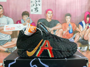 Side view of a black LeBron 12 shoe with orange and red accents.