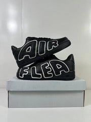 Stacked view of two black low-top sneakers displaying oversized outlined AIR and FLEA side lettering.