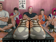 Front view of white and grey Nike sneakers with orange-trimmed panels and dark brown laces.