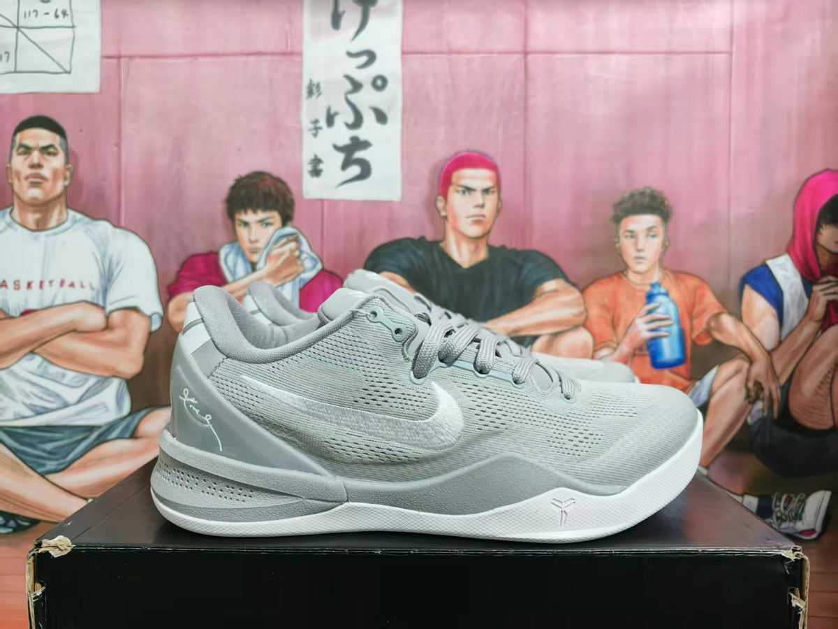 Gray and white Nike basketball sneakers shown from the side on a black box, with a basketball-themed illustrated backdrop.