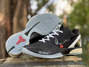 Black sneaker pair with one outsole facing upward, revealing a translucent traction pattern and red Kobe logo detail.