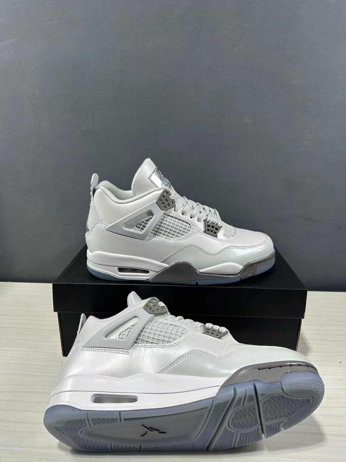 Side view of grey Jordan Air Jordan 4 sneakers displayed above a shoebox, showing the mesh panels, lace supports and translucent outsole.