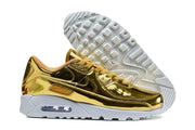 Gold-tone Nike Air Max 90 QS sneakers showing the side profile and patterned outsole.