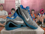 Angled view of the pair of gray and blue Nike basketball sneakers highlighting the white Swoosh and blue speckled outsole.