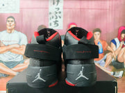 Rear view of the black and red sneaker pair showing ankle straps, red collar trim, heel branding, and red outsole accents.