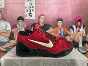 Side profile showing the light-colored Swoosh, perforated red upper, black speckled heel section, and black outsole.