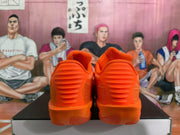 Rear view of bright orange Nike sneakers showing padded heel sections, layered heel detailing, and translucent orange outsoles.