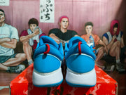 Rear view of blue and white Nike basketball sneakers with red pull tabs, displayed on an illustrated red shoebox.