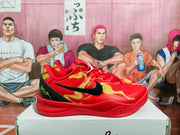 Side view of red Nike basketball sneakers with gold graphics, a black Swoosh, and black heel panels on a shoe box.