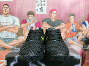 Front view of black Nike sneakers with black laces, textured panels, and small light-colored tongue markings.