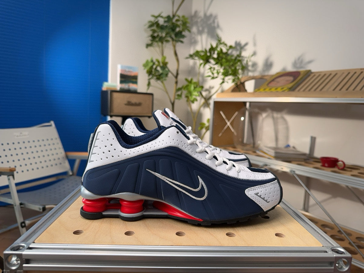 White and navy Nike Shox-style sneaker with a Swoosh and red heel cushioning elements