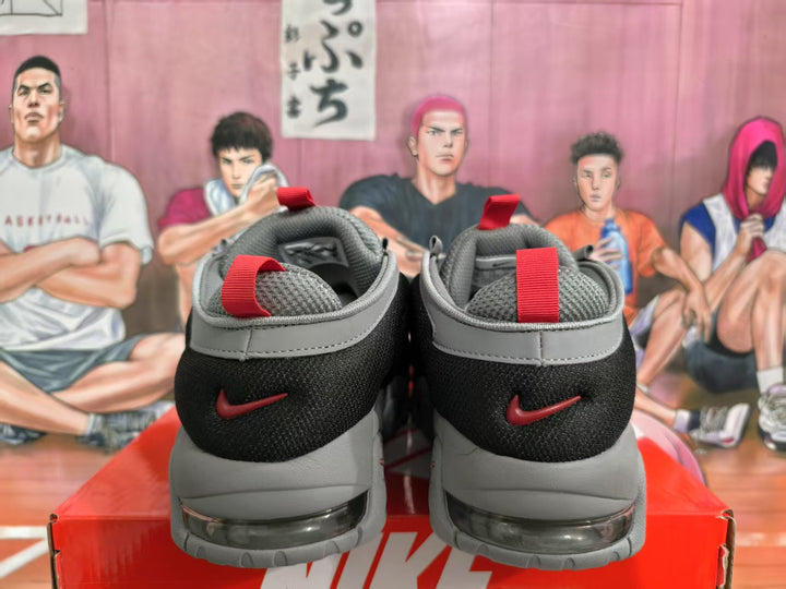 Rear view of gray and black Nike sneakers with red heel pull tabs and red heel branding, displayed on a red shoebox.
