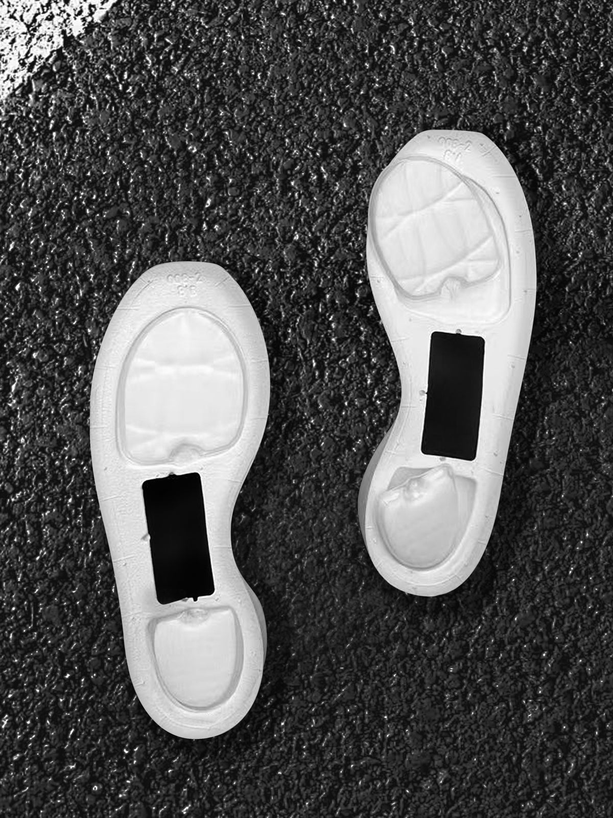 Underside view of two white sole components with recessed cushioning areas and black rectangular sections.